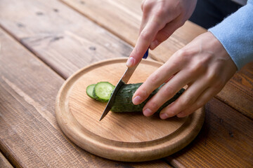 hands of a girl cut cucumber on a wooden table, the process of making vegetarian salad, close-up cutting of vegetables and greens