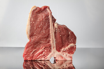 Raw t bone steak is on a wooden Board on black background, next to salt, pepper and herbs.