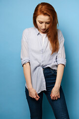 A red-haired girl in a striped shirt stands on a blue background and, with her head bowed, holds...