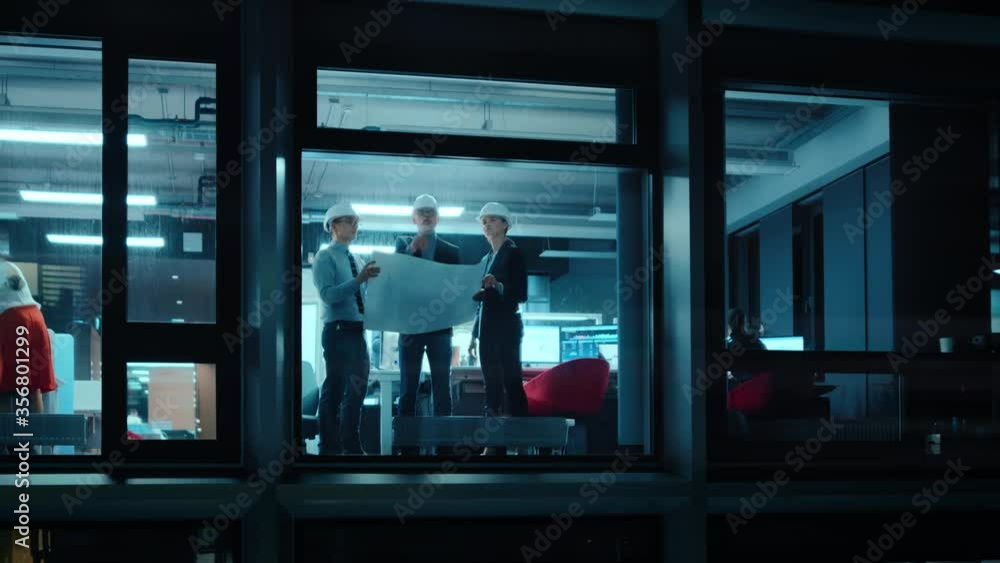 Poster Footage from Outside the Window: Architects and Engineers in Hard Hats Stand Next to a Window in Office Workplace and Look at Blueprints on Paper. Senior Specialists Explains the Job to His Apprentice