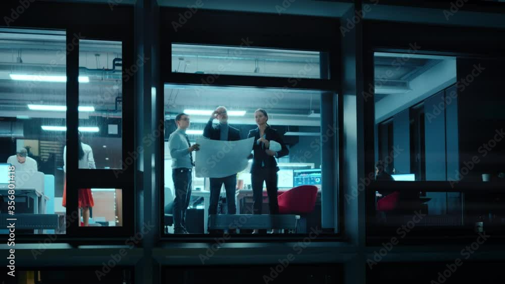 Poster Footage from Outside the Window: Architects and Engineers with Hard Hats Stand Next to a Window in Office and Look at Blueprints on Paper. Senior Specialists Explains the Job to His Apprentice.