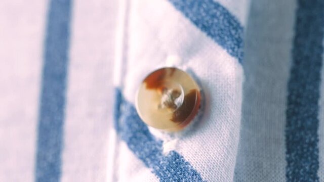 Closeup of a classic shirt button being fastened up using hands .