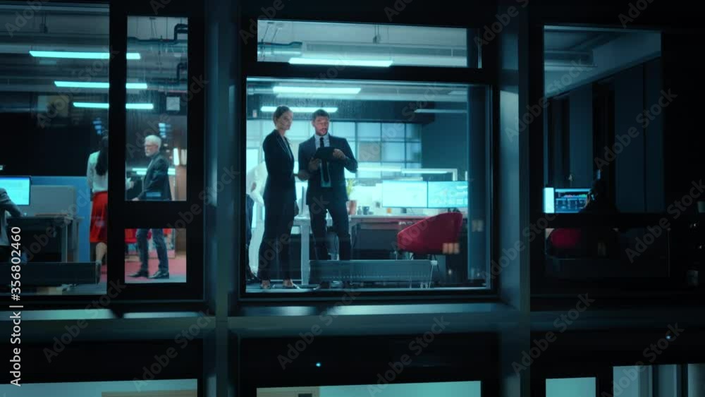 Poster Footage from Outside: Two Business Partners Use a Tablet Computer Next to Window in the Office. Employees Talk about Financial Strategies and Business Development. Colleagues Work Behind Them.