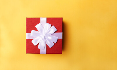 Decorative red gift box with white ribbon on yellow background. Top view. Space for text