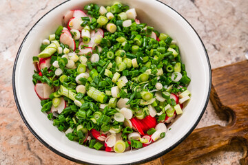 Salad with radish and onion in white metal plate on the table near wooden cutboard