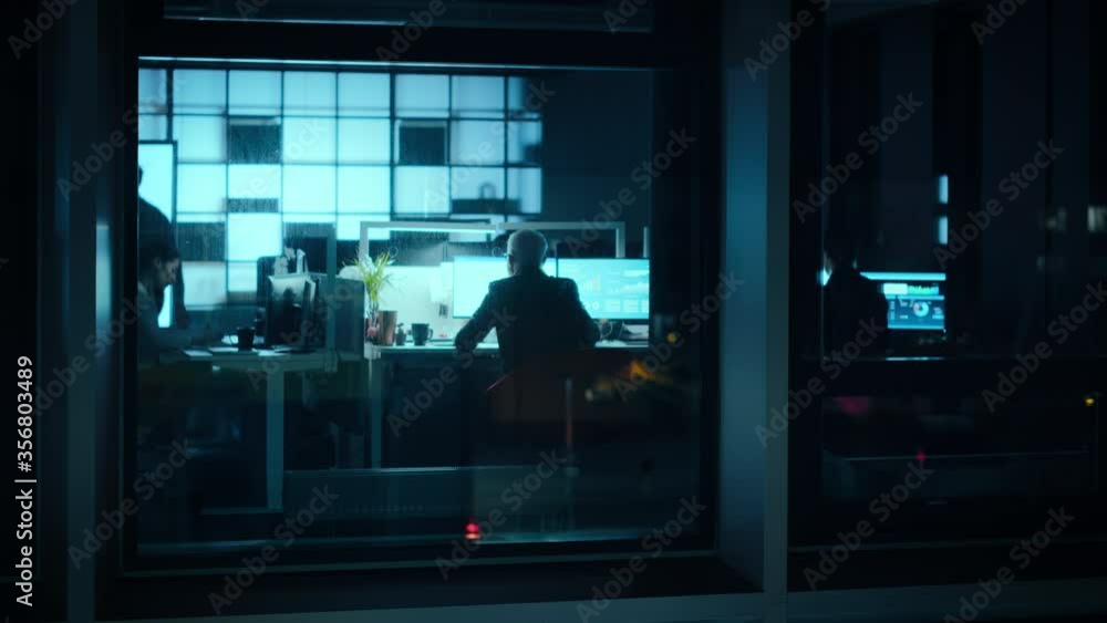 Poster footage from outside the window: senior businessman sitting in front of a desk computer in his offic
