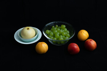 Various fresh fruits on black background.Red nectarine in white dish and yellow peach on black...
