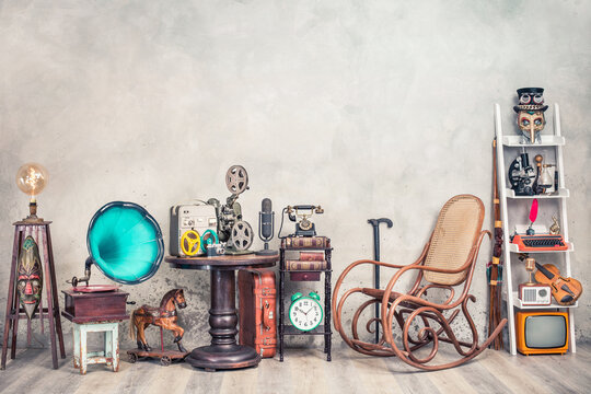 Antique gramophone, rocking chair, old typewriter, retro radio, tape recorder, projector, books, clock, camera, fiddle, mask, cylinder hat, cane, suitcase, bow. Vintage style filtered photo