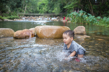 cute little baby boy playing water in the shallow river alone during family holiday in summer season