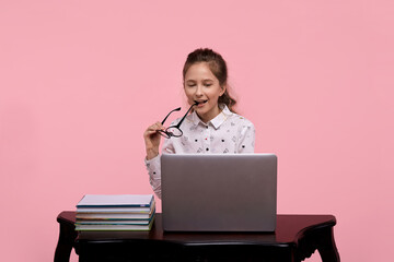 cheerful girl is sitting at a laptop, holding glasses in the corner of her lips