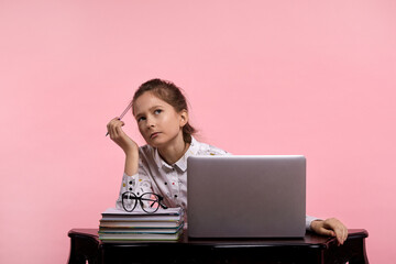 A young beautiful girl of Caucasian appearance is thinking over her homework.