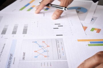 The hand is holding the pen and analyzing the graph, 
Businessman analyze graph report on table