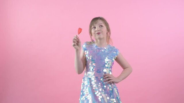 Happy girl in dress twists in his hands candy on a stick in the shape of a heart