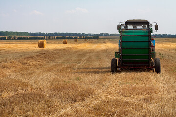Obraz premium A tractor with a trailed bale making machine collects straw rolls in the field and makes round large bales