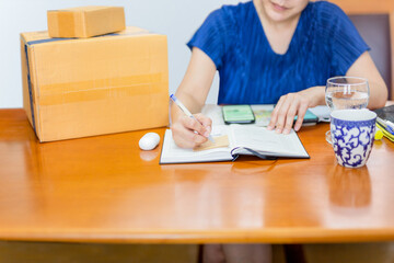 Woman write paper note for delivery package to customer from home office.