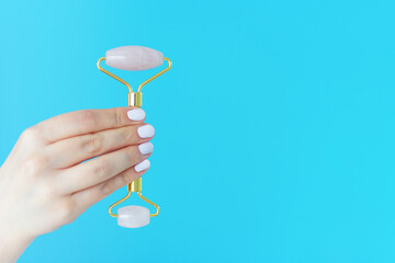 A woman's hand with a white manicure holds facial massage roller on a blue background