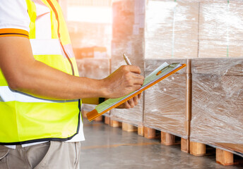 Warehouse worker hand writing checklist on clipboard. cargo shipment boxes pallet, warehouse inventory management.