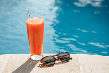 Summertime orange juice  and sunglasses relax near swimming pool. Summer vacation near swimming pool