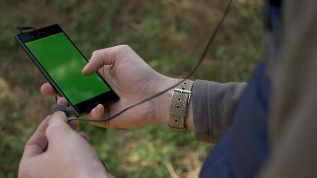 A hiker chooses a song to listen to on his woodland walk and puts in his earphone