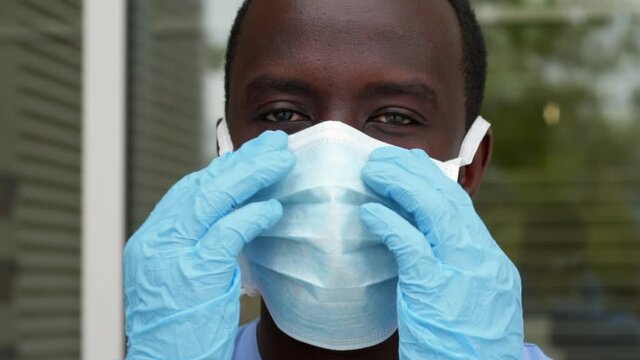 Close Up Of African American Black Male Nurse Doctor Putting On PPE Medical Mask Blue Medical Wearing Gloves. Slow Motion, HD.