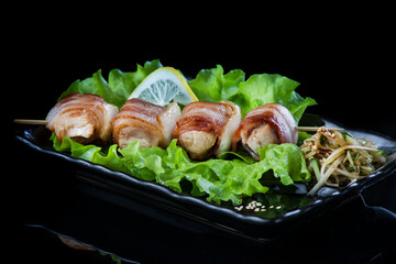 meat on wooden skewers, pork, chicken, fish, scallop, beef, shrimp in a black plate on a black background.
