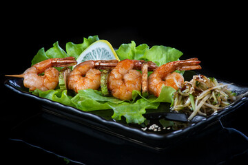 meat on wooden skewers, pork, chicken, fish, scallop, beef, shrimp in a black plate on a black background.