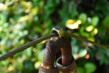 A close up image of a wire boundary rope welded to a metal pole to create a safety boundary in a wooded area. 