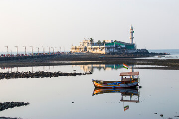Fototapeta premium Mumbai India Nov 9th 2019: an old fishing boat anchors in the Haji Ali Bay with India flag on the top. The background is Pir Haji Ali Shah Bukhari, a mosque and dargah (tomb) or the monument