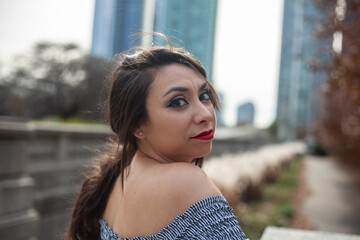 young beautiful fashion Latina woman wearing a trendy blue skirt is enjoying the outdoor park in the Chicago downtown metropolitan area. autumn is here as the color of the trees have change red 