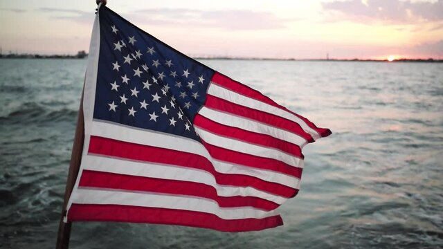 Patriotic American Flag flapping flying in wind from transom of boat on bay with sunset in background Memorial Day Fourth of July Independence Day Veterans Day Presidents Day