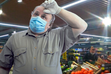 A man in a short-sleeve shirt, medical mask and gloves wearily wipes the sweat from his forehead with his hand