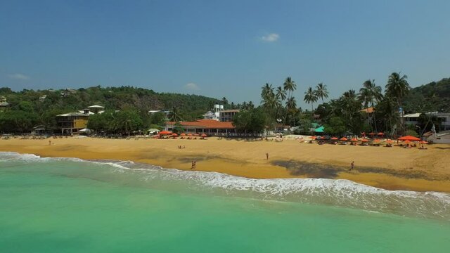 Aerial panning shot of people at beach against sky on sunny day, drone flying over sea - Arugam Bay, Sri Lanka
