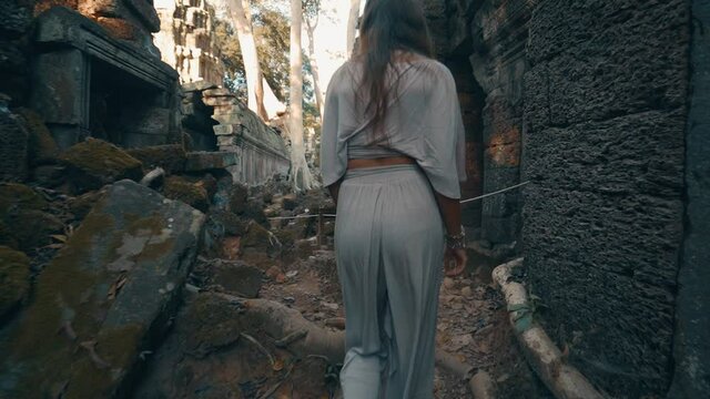 A young woman walking amongst the toppled stone ruins of Ta Prohm Temple, Cambodia, slow motion