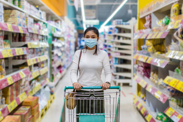 asian woman with shopping cart in supermarket department store and her wearing medical mask for prevention coronavirus(covid-19) pandemic. new normal concept
