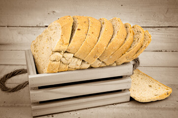 Fresh whole wheat bread cut into pieces in a wooden box and with a wooden background.