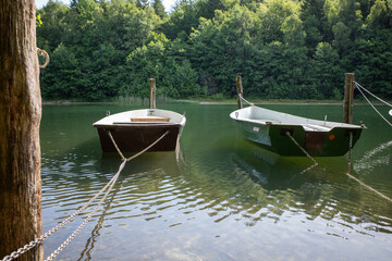 some Rowboats are moored on the shore of a lake with chains