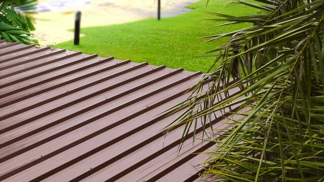 Corrugated metal roofing in brown paint color,4K video.
Rust resistance corrugated aluminium roofing and surface in the  garden after the rain ,high angle view with palm leafs in foreground .