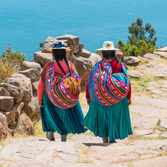 Indigenous Peruvian Quechua women in traditional clothing walking down steps on Taquile Island, Titicaca Lake, Peru. - obrazy, fototapety, plakaty