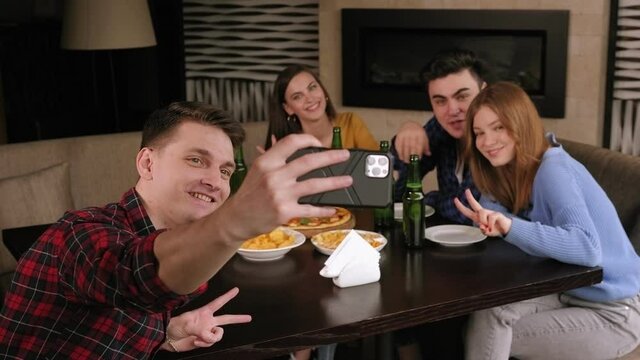 A group of cheerful friends relax in a cafe, eat pizza and chips, drink beer and take selfies. Friends are photographed as a memento of a meeting in a pizzeria. Meeting old friends.