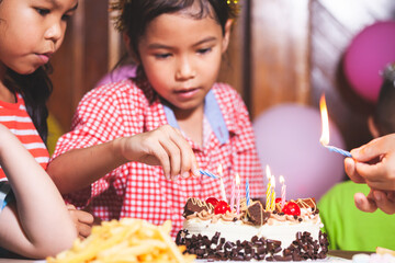 Asian children girls and boys lighting candle on birthday cake together in birthday party