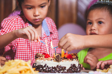 Asian children girls and boys lighting candle on birthday cake together in birthday party