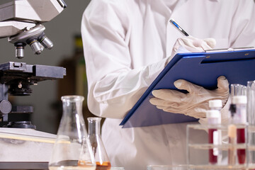 Asian scientist is writing data after analysis and research chemical test in a laboratory.