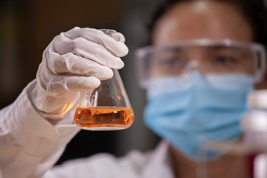 Asian Scientist Is Holding A Test Tube With Orange Liquid Chemical For Analysis And Research Chemical Test In A Laboratory.