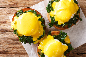 Benedict eggs with spinach and hollandaise sauce on a toasted bun close-up. Horizontal top view
