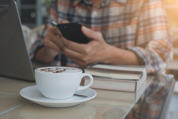 Man working on laptop computer and using smartphone at coffee shop