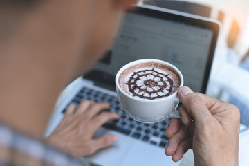 Man drinking coffee while online working on laptop computer