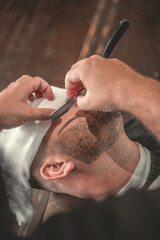 Barbeiro fazendo a barba do seu cliente na sua barbearia, imagem de close no rosto usando navalha