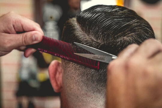 Barbeiro cortando cabelo do seu cliente da sua barbearia no estilo vintage, usando tesoura e navalha e m&aacute;quina de cortar barbeador el&eacute;trico e pente