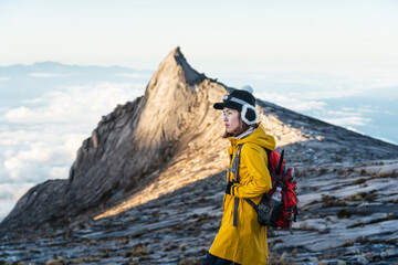 Young woman trekker with backpack standing in front of South peak of Kinabalu mountain massif, Borneo island in Sabah state, Malaysia