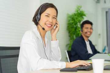 close up asian call center woman agent wear headset device and smiling working in operation room with service-mind at desktop table , telemarketing and help desk concept	
